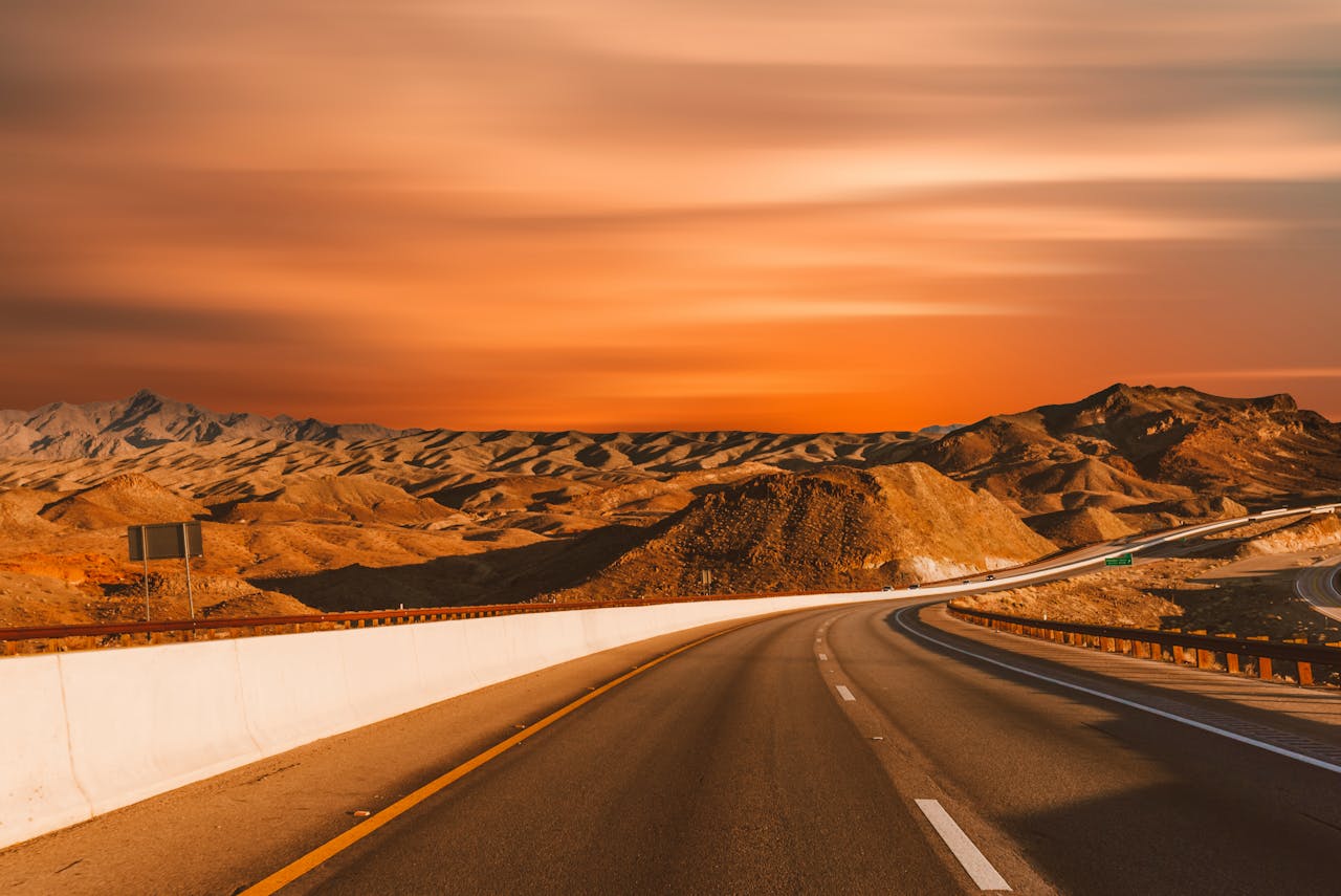 Empty highway winding through desert hills under a stunning sunset sky.